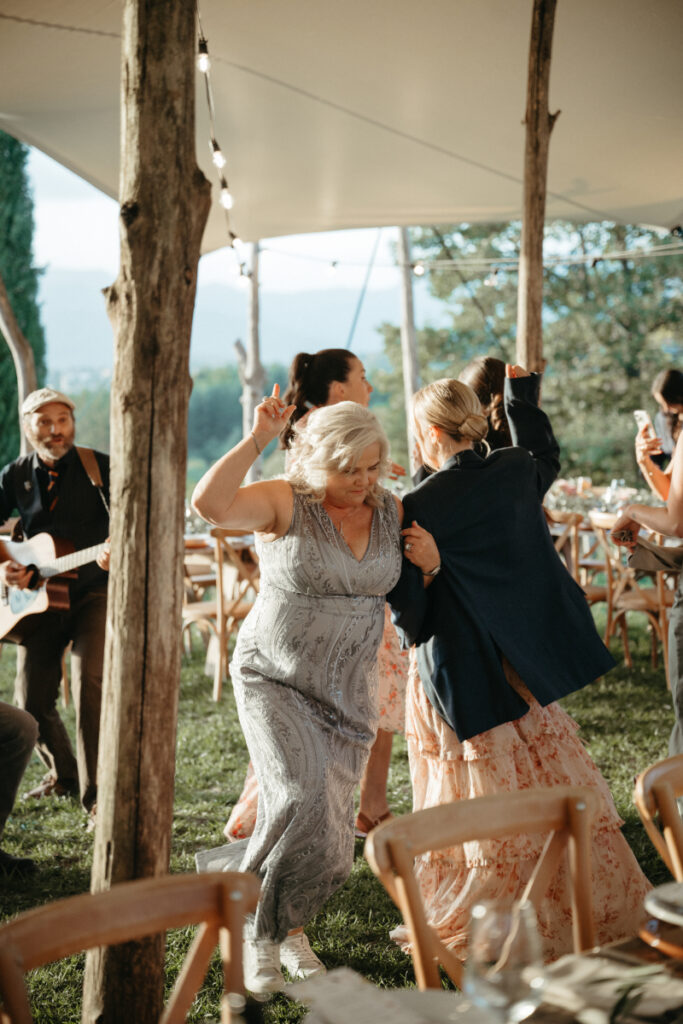 The mother of the groom and a bridesmaid share a joyful moment, laughing and dancing together on the reception dance floor.