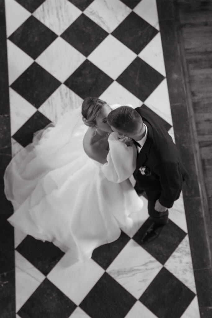 Bride and groom kiss as they stand on a checkered aisle. 