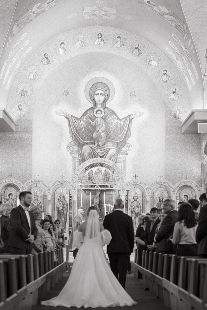 Bride walks with father down the aisle of a church to her soon to be husband.