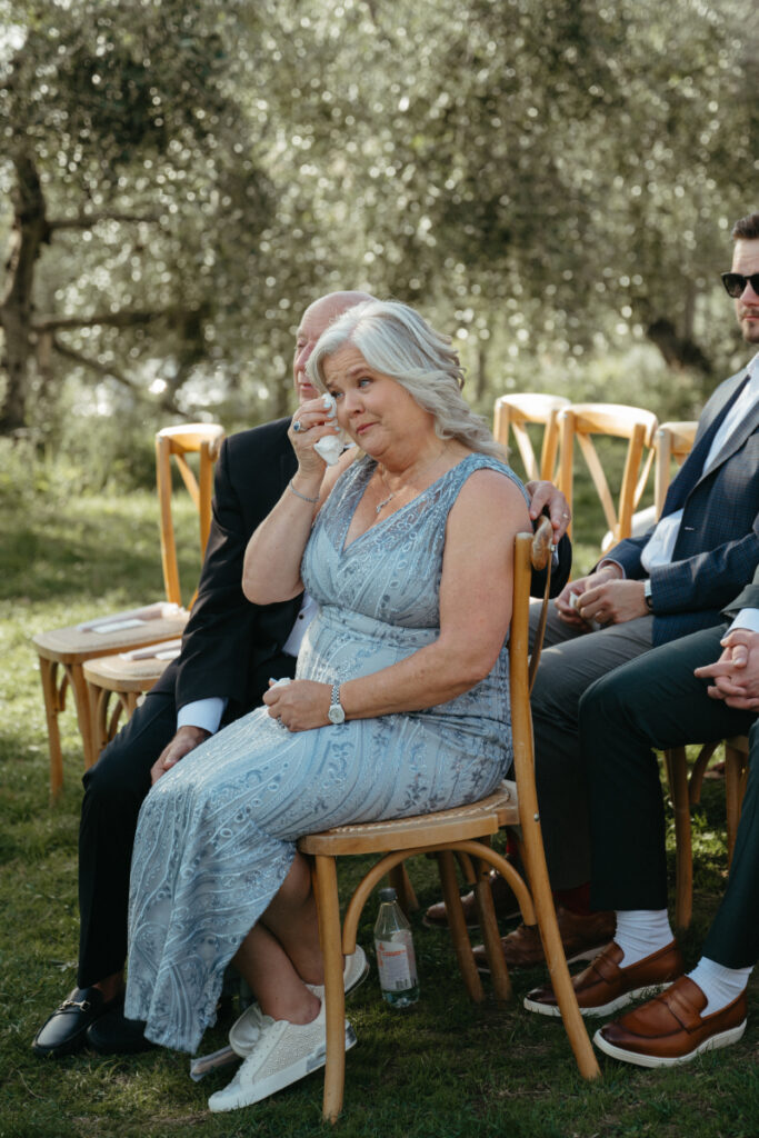 The mother of the groom wipes happy tears with a tissue as she watches the ceremony with a heartfelt smile.