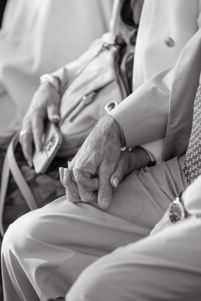 An elderly couple holds hands lovingly during a wedding ceremony.