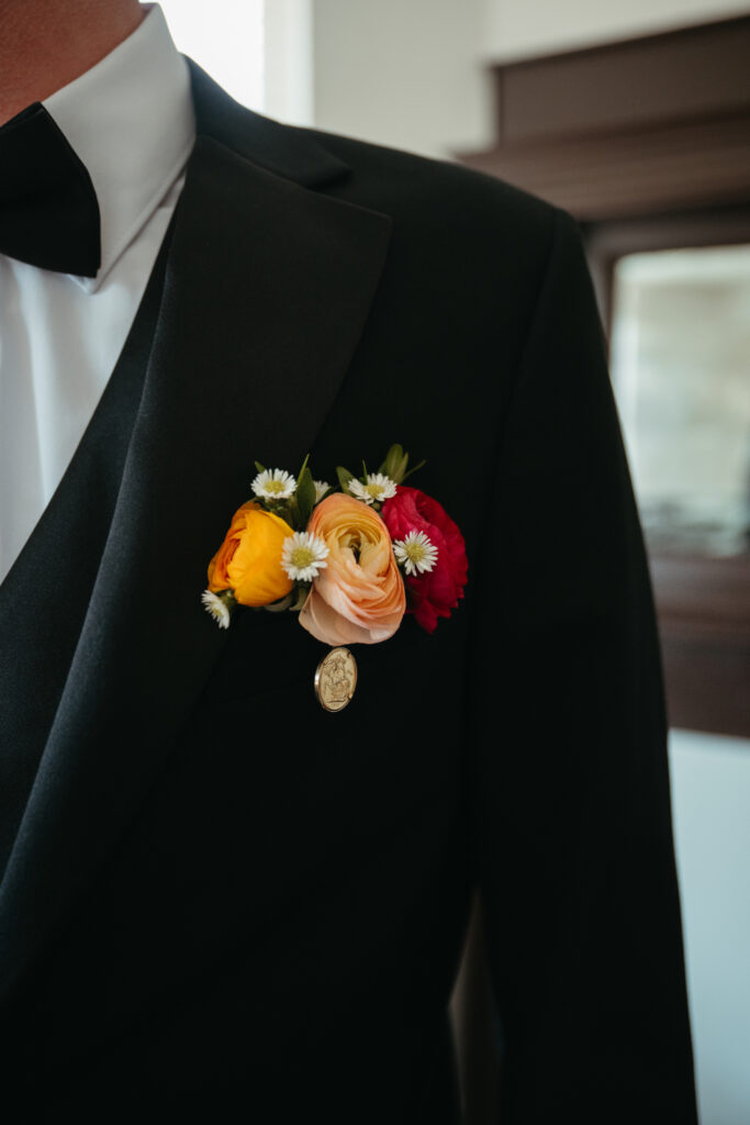 close up of grooms black and white tuxedo and red, orange and peach boutonniere