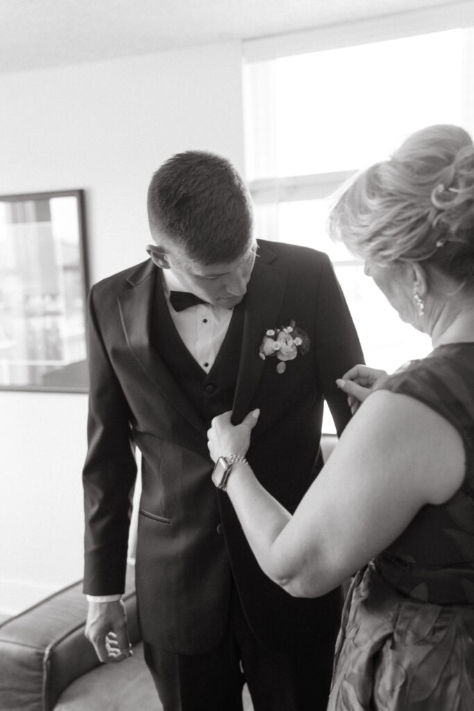 black and white of mother of groom adjusts his boutonniere