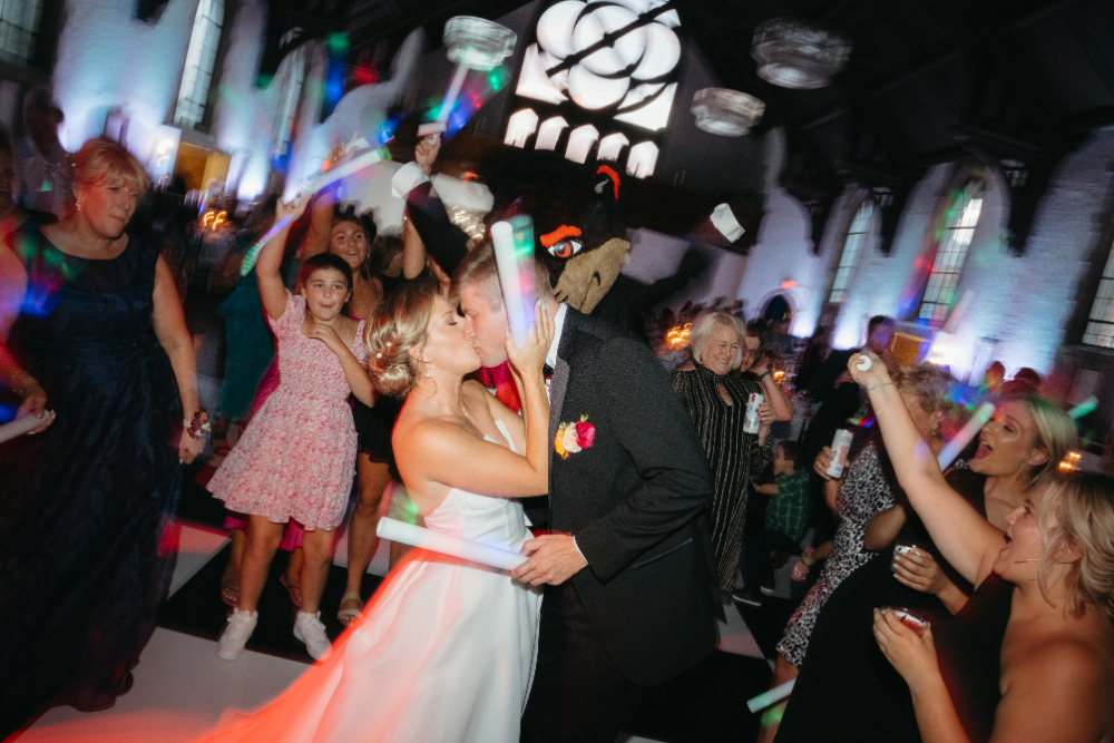 bride and groom share a kiss while wedding guests celebrate around them