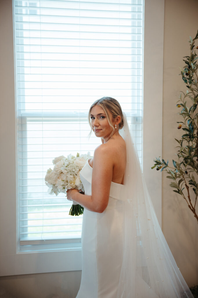 Bride posing by a window with bouquet.