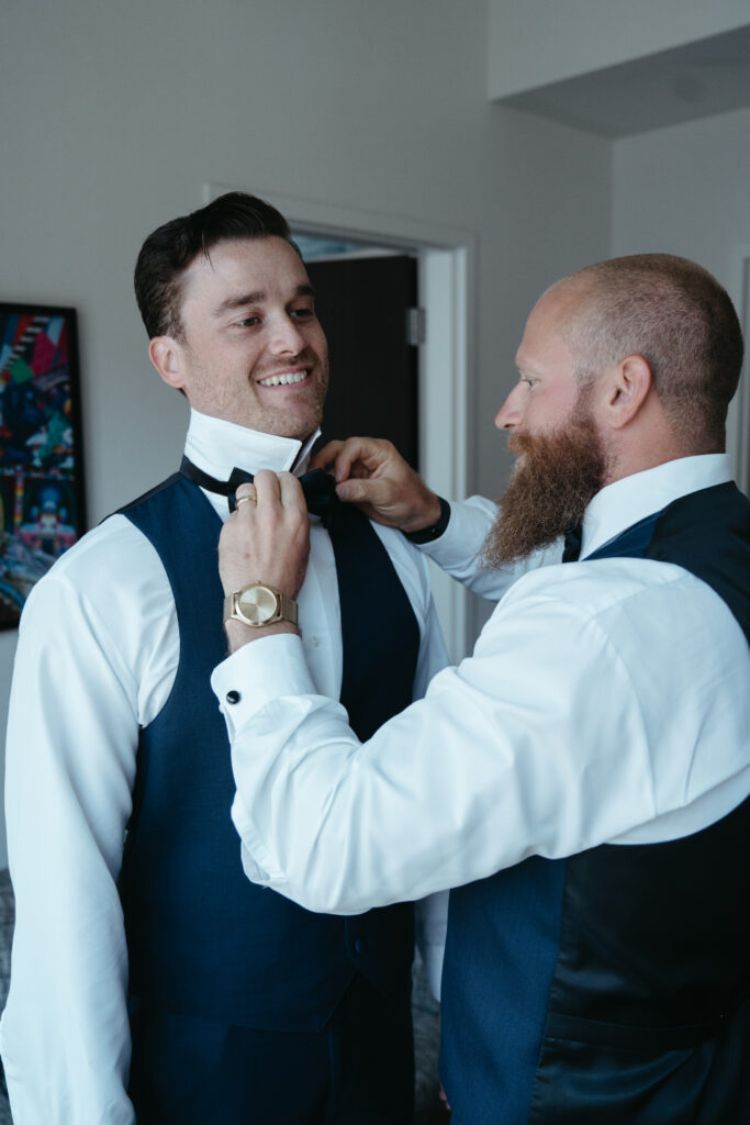 Groomsman adjusting groom’s bow tie.