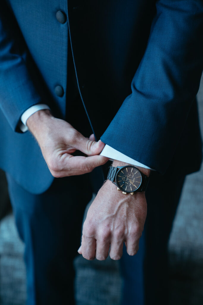 Groom buttoning navy suit jacket, wearing a black watch.