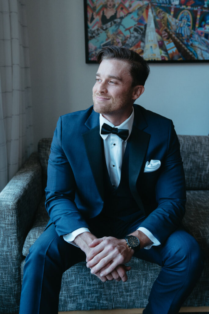 Groom sitting in a navy tux, smiling.