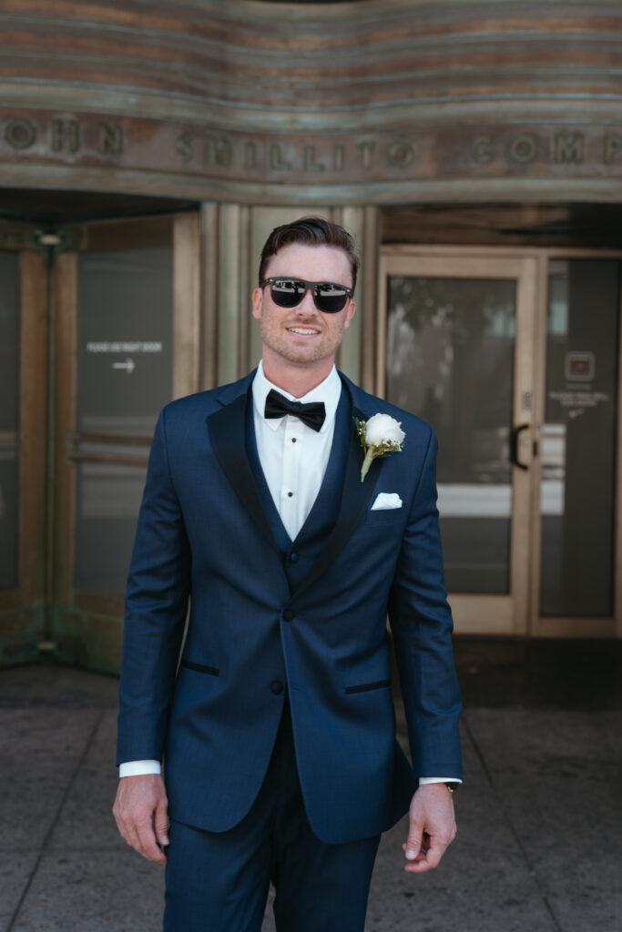 Groom in sunglasses outside a historic building.