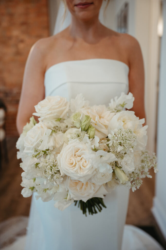 Bride holding a bouquet of white roses and baby’s breath.