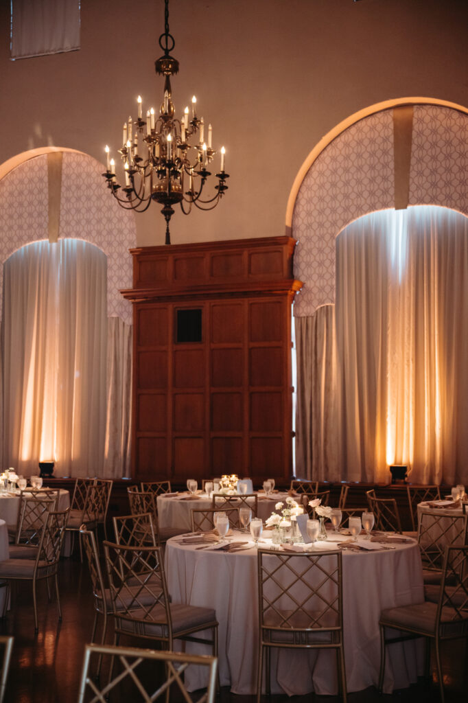 Candlelit tables and gold chairs under chandeliers.

