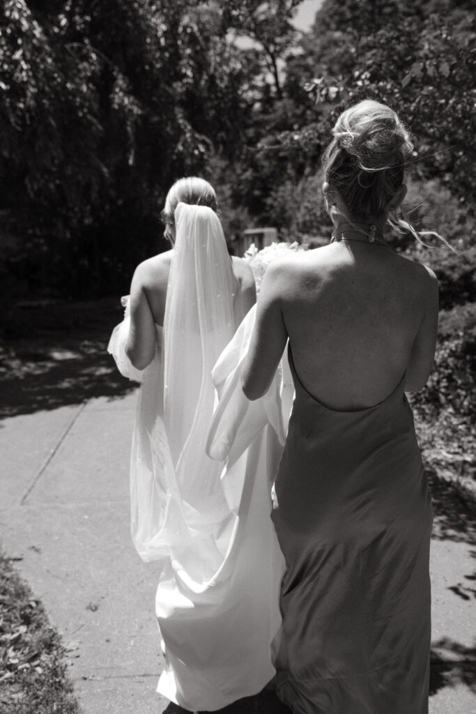 Bride and bridesmaid walking outdoors in black and white.
