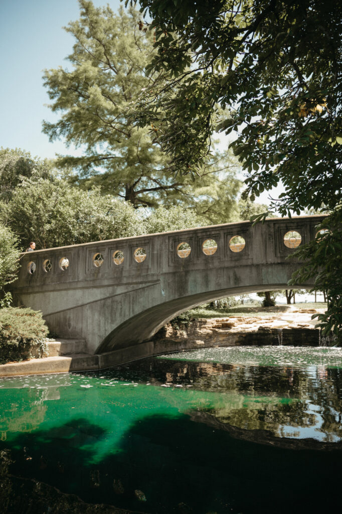 Stone bridge over a pond with trees in the background.
