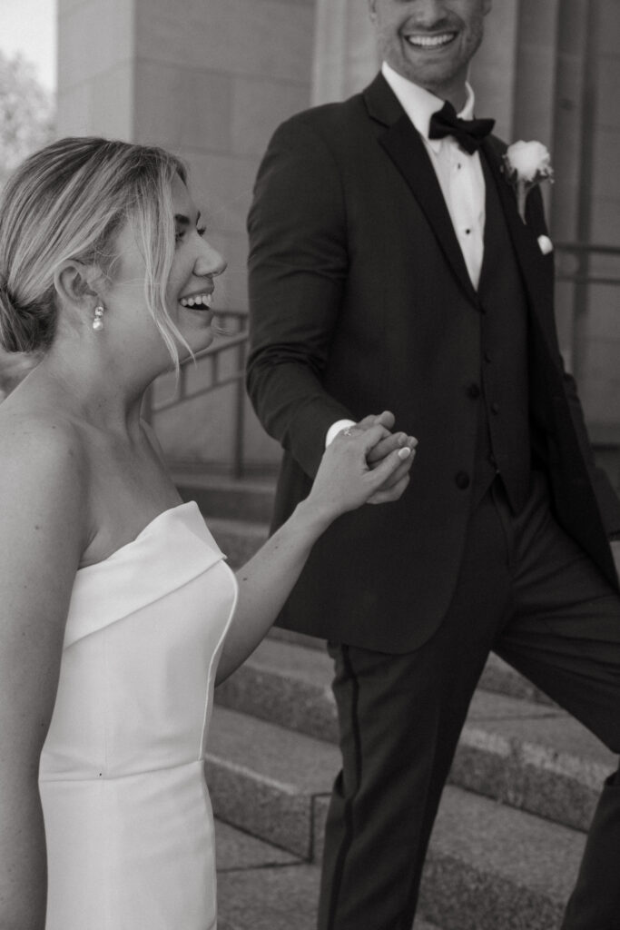 Bride laughing while holding groom’s hand.
