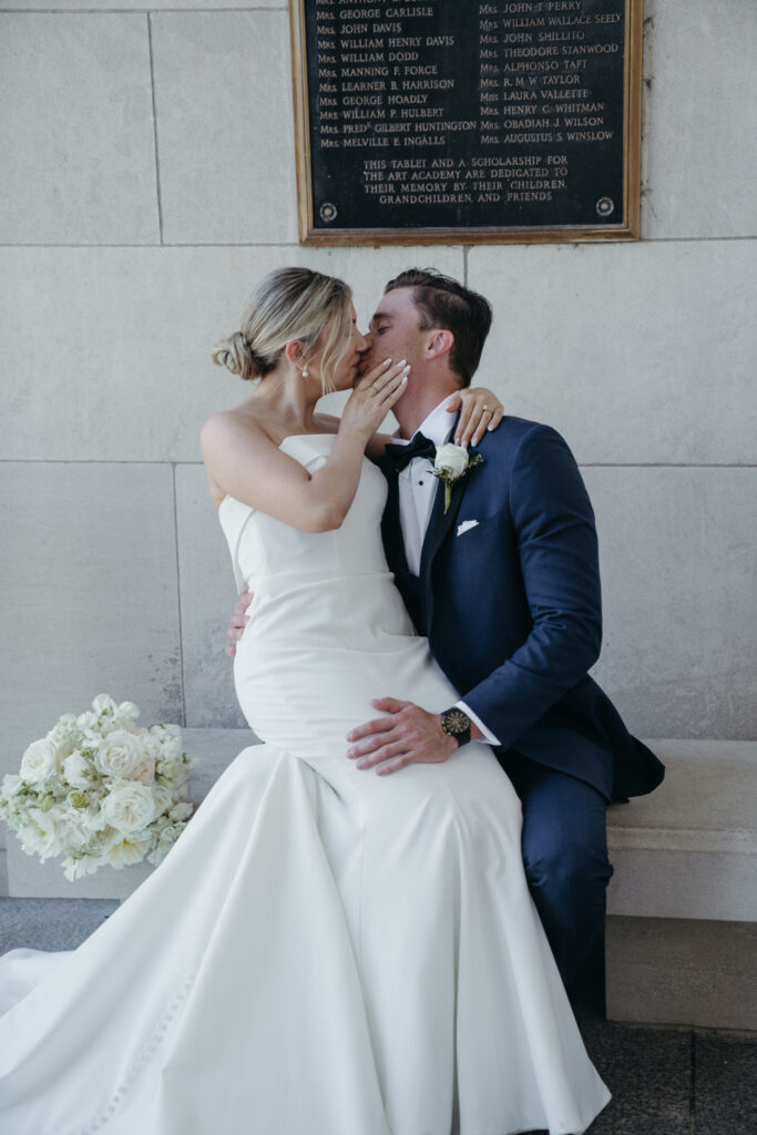 Bride and groom kissing on a stone bench.
