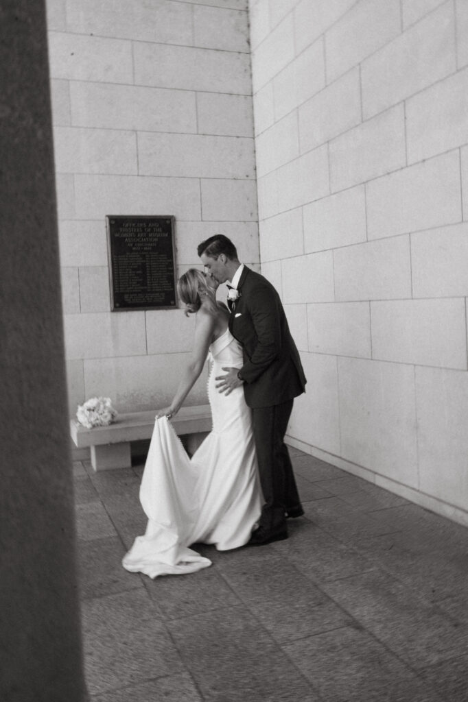 Black and white photo of couple kissing near a stone wall.
