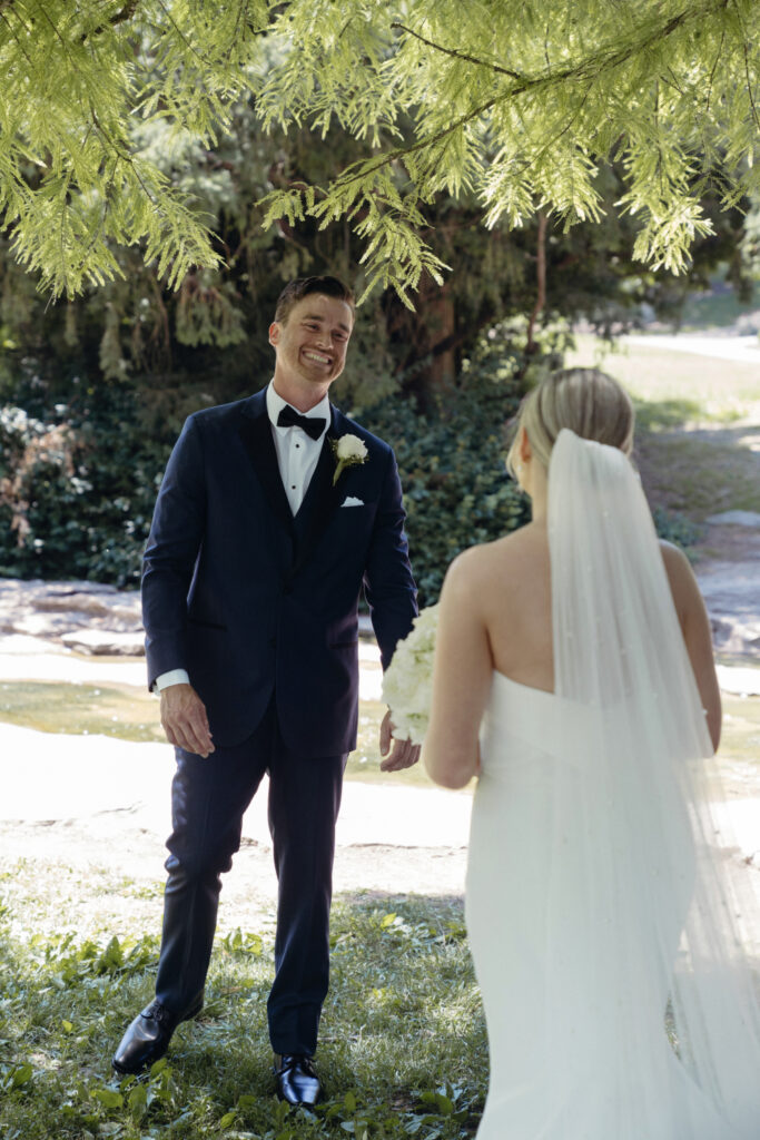 Groom smiling at bride under tree.
