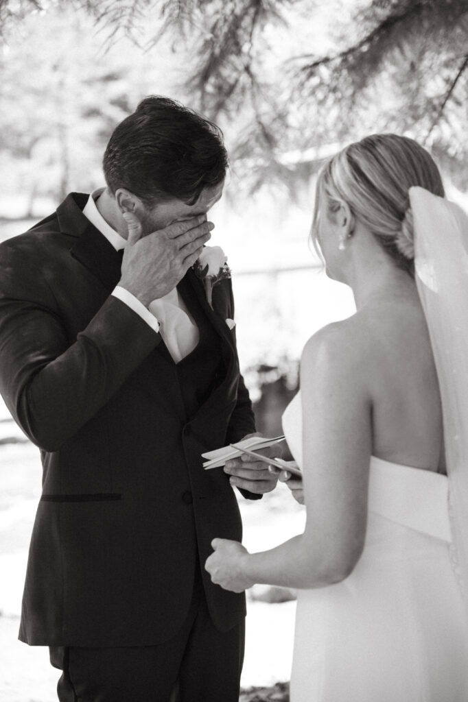 Groom wiping tears while holding vows.
