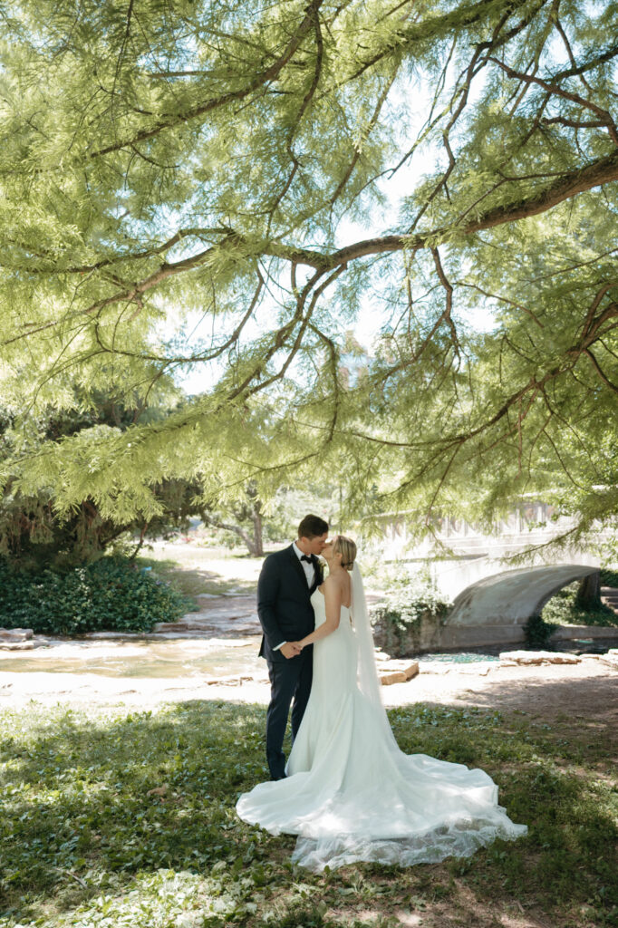 Bride and groom kissing under tree.
