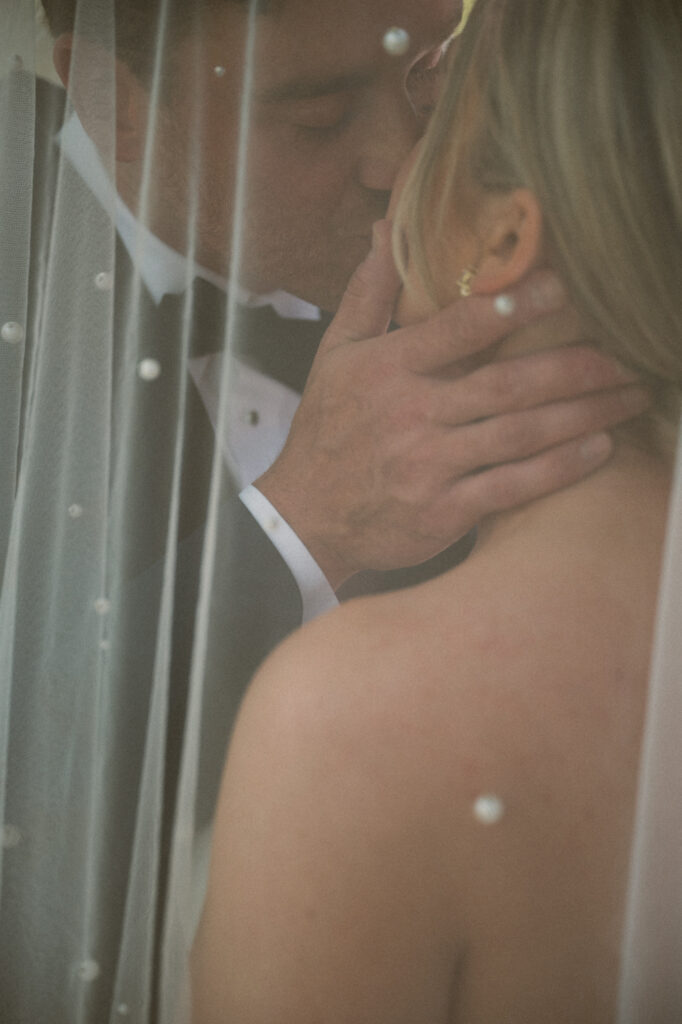 Close-up of groom kissing bride under veil.
