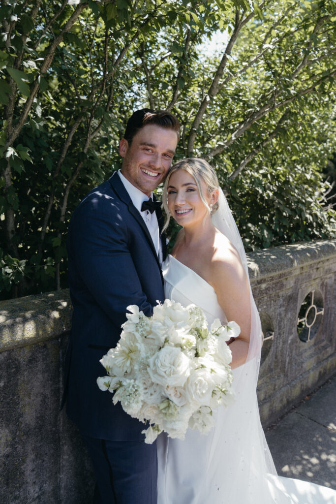 Bride and groom smiling by a stone railing.
