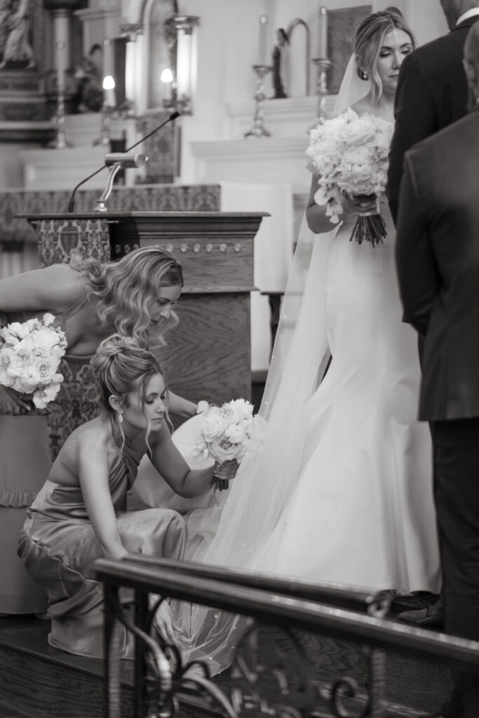 Bridesmaids adjust the bride’s dress and veil at the altar.
