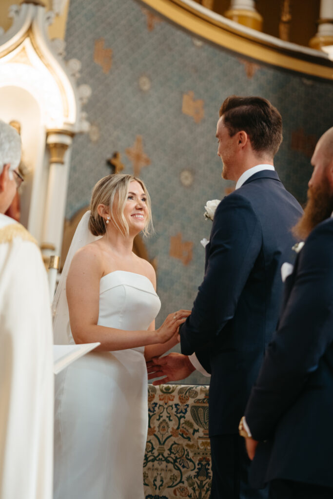 Bride smiles at the groom while holding hands during the ceremony.
