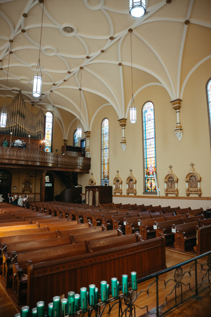 Interior of St Rose Catholic Church with wooden pews, stained glass windows, and vaulted ceiling.