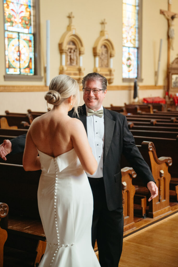 Bride and father embrace inside St Rose Catholic Church near wooden pews.
