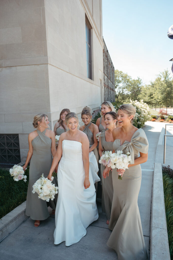 Bride and bridesmaids walking and laughing outdoors.
