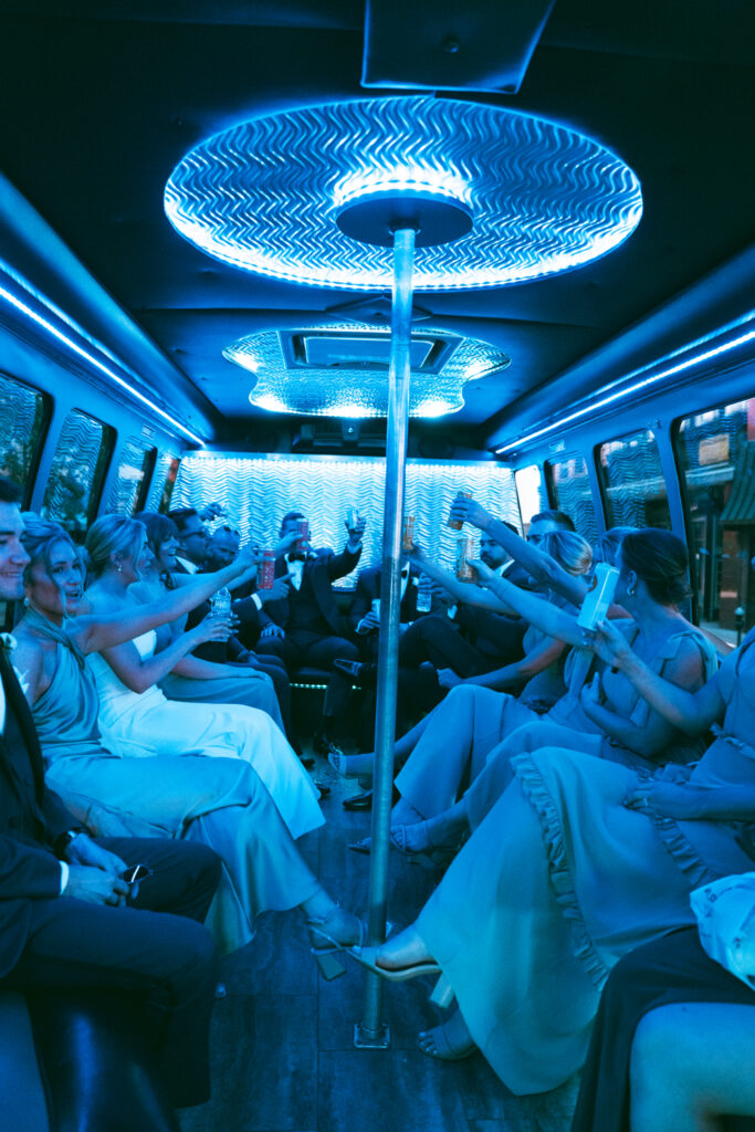 Wedding party raising drinks inside a party bus with blue lighting.
