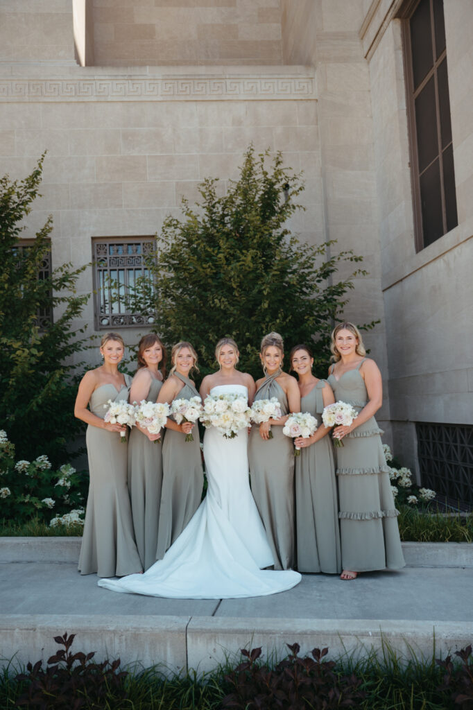 Bride with bridesmaids in sage dresses holding white bouquets.
