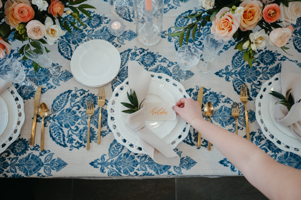 wedding-planning-secrets close up of the reception table details, blue and white table cloth with peach colored florals and gold cutlery