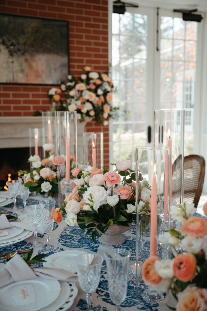 wedding-planning-secrets a brick fireplace backdrop and the table is adorned with lush floral arrangements in soft shades of peach, blush, and ivory, paired with tall blush taper candles in clear glass holders- wedding planning secrets
