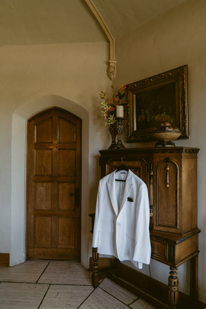 A crisp white tuxedo jacket hangs in a vintage room, styled with timeless, old-world charm.