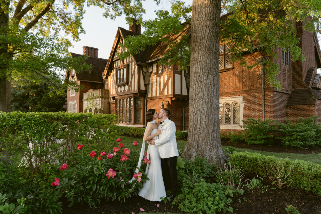 The couple embraces beneath the trees, with Pinecroft at Crosley Estate glowing in golden hour light.