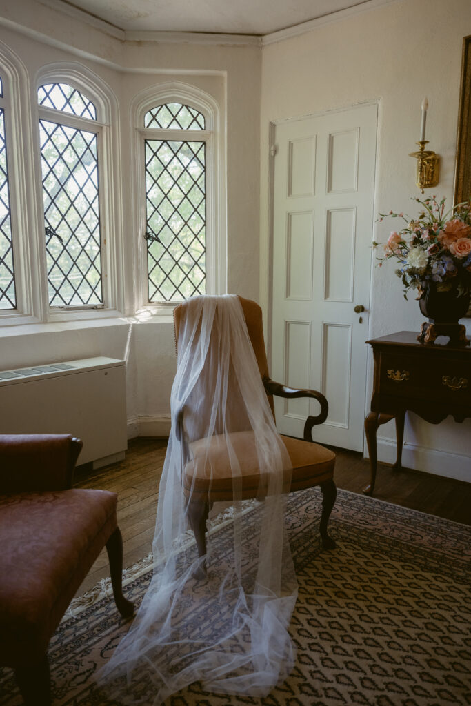 A crisp white tuxedo jacket hangs in a vintage room, styled with timeless, old-world charm.
You said:
ChatGPT said:
A delicate bridal veil drapes over a vintage chair, softly lit by leaded windows and morning light.