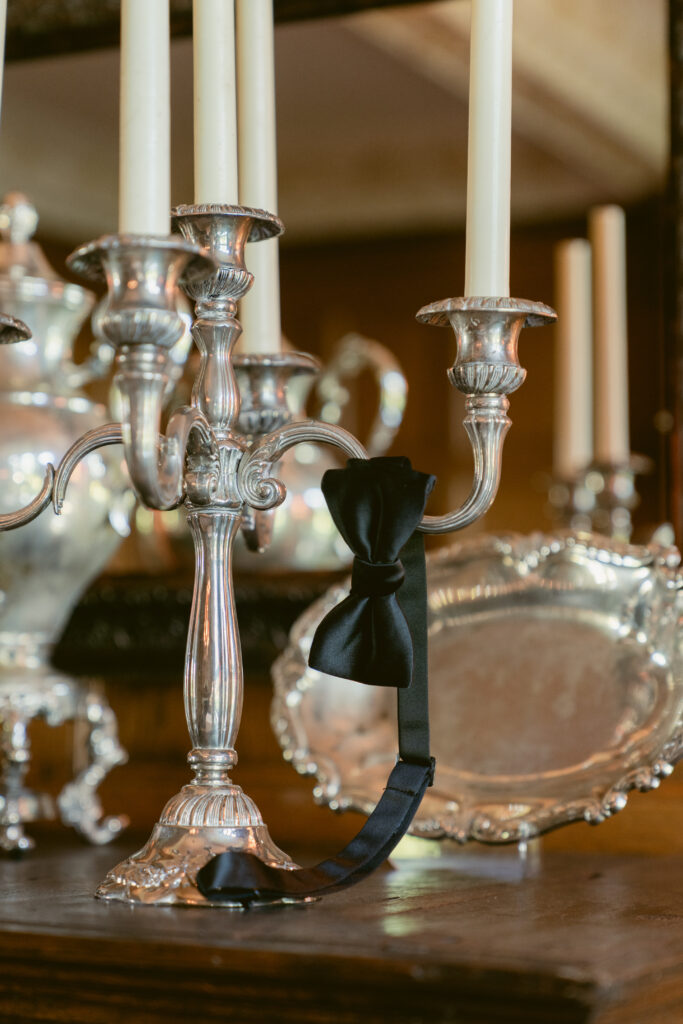 A black bow tie drapes elegantly over a vintage silver candelabra, surrounded by polished heirloom décor.