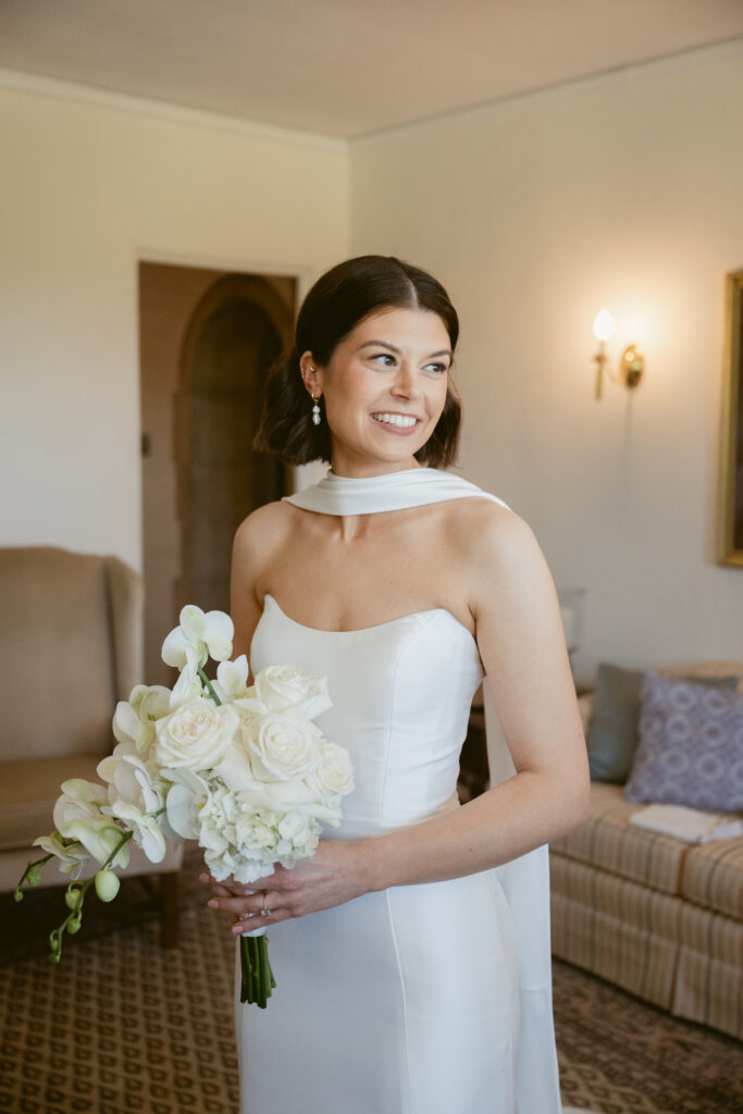 The bride glows in a sleek satin gown, holding a white bouquet of orchids and roses.