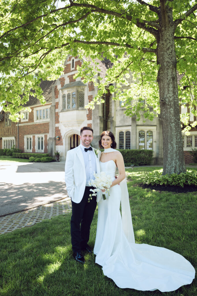A joyful couple poses outside Pinecroft at Crosley Estate, embracing timeless elegance and vibrant summer light.