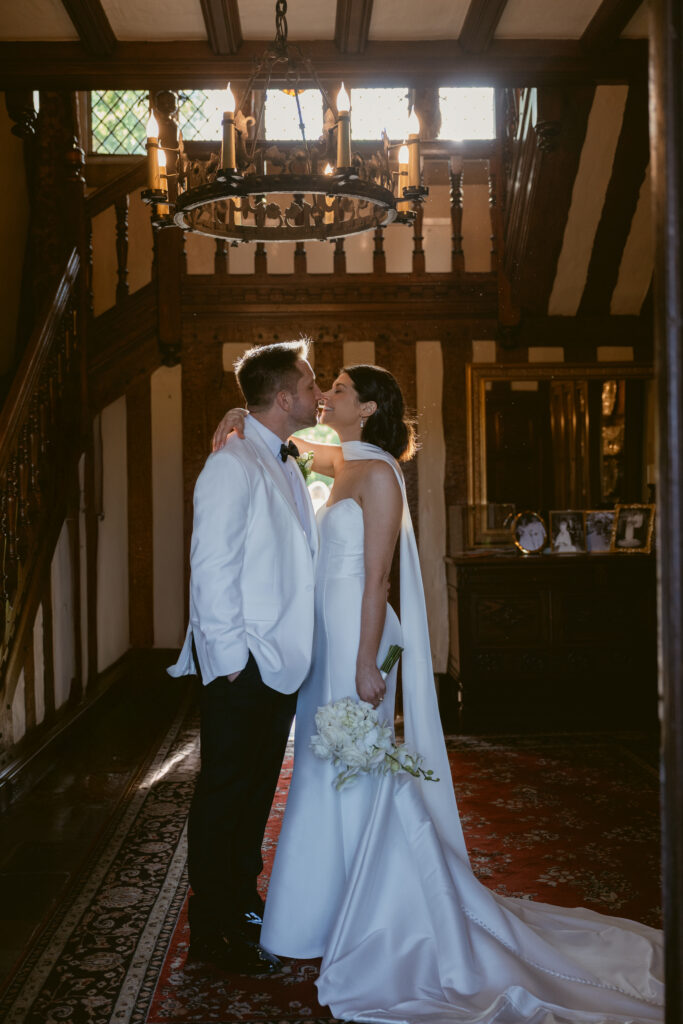 The couple shares an intimate moment in a grand foyer, kissed by warm light and elegance.