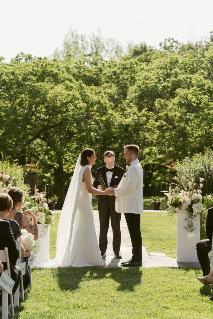 The couple exchanges vows in a sunlit garden ceremony, surrounded by flowers and loved ones.