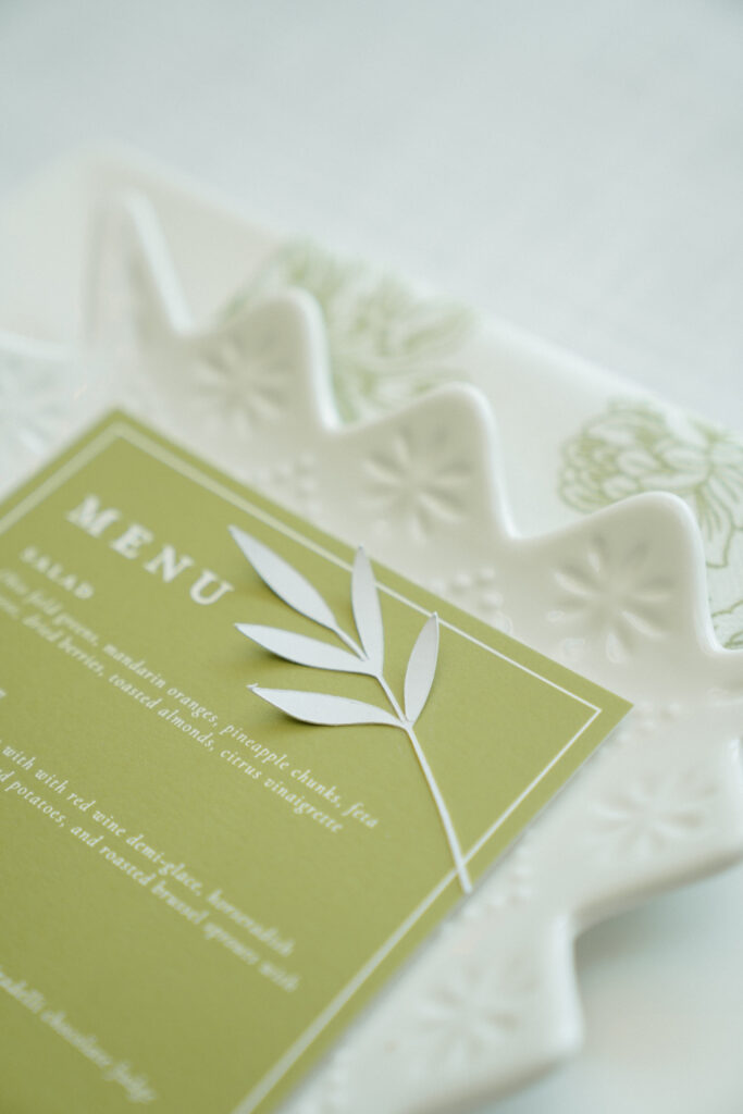 Green wedding menu card with white leaf detail on a white textured plate.