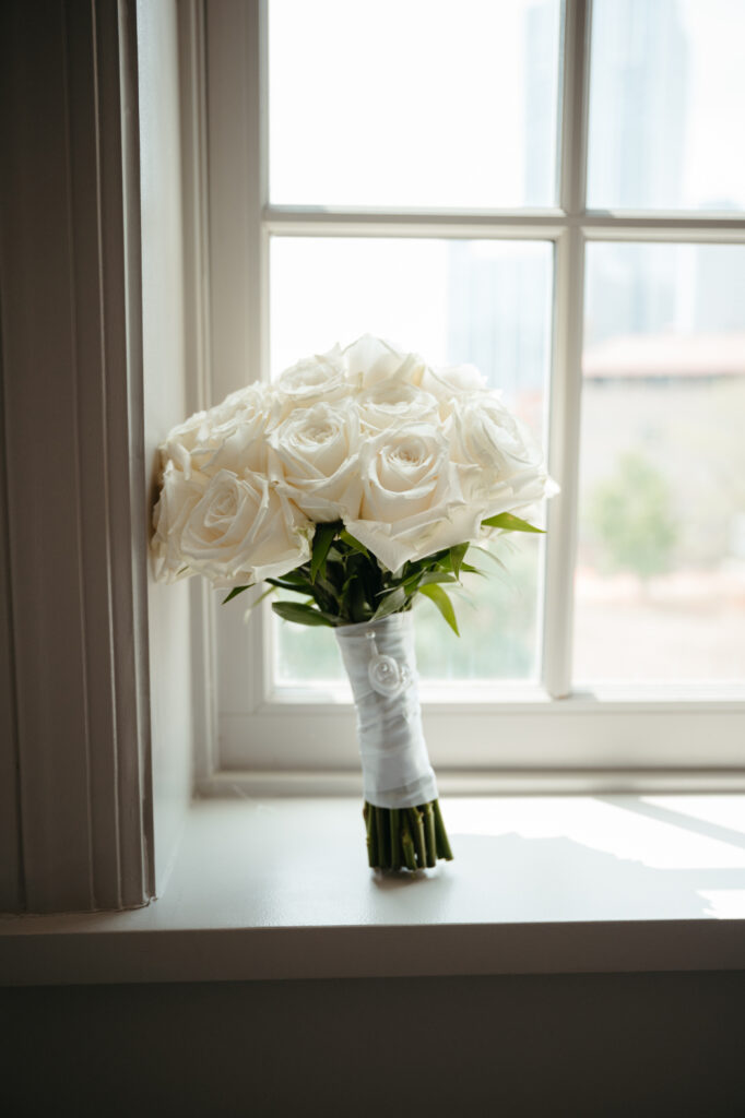 wedding-color-palette Classic bridal bouquet of pristine white roses rests softly on a sunlit windowsill, simple elegance.
