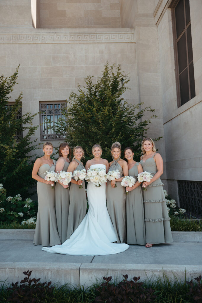 wedding-color-palette Bride and bridesmaids showcase a chic wedding color palette with muted sage dresses and creamy bouquets.