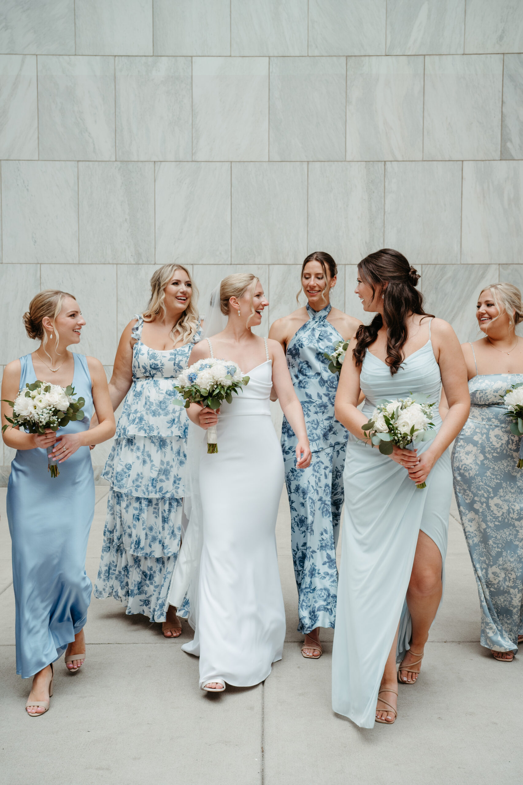 bridesmaids and brides looking at each other with joy dressed in blues and whites