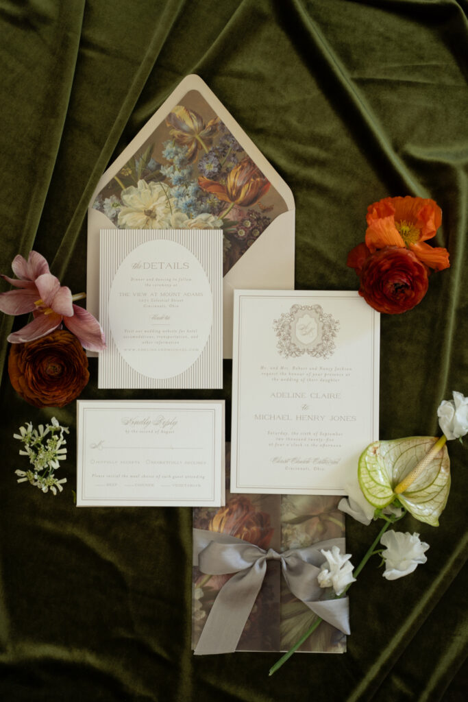 Flatlay of floral wedding invitations on olive velvet with bold flowers in rich red and blush tones.
