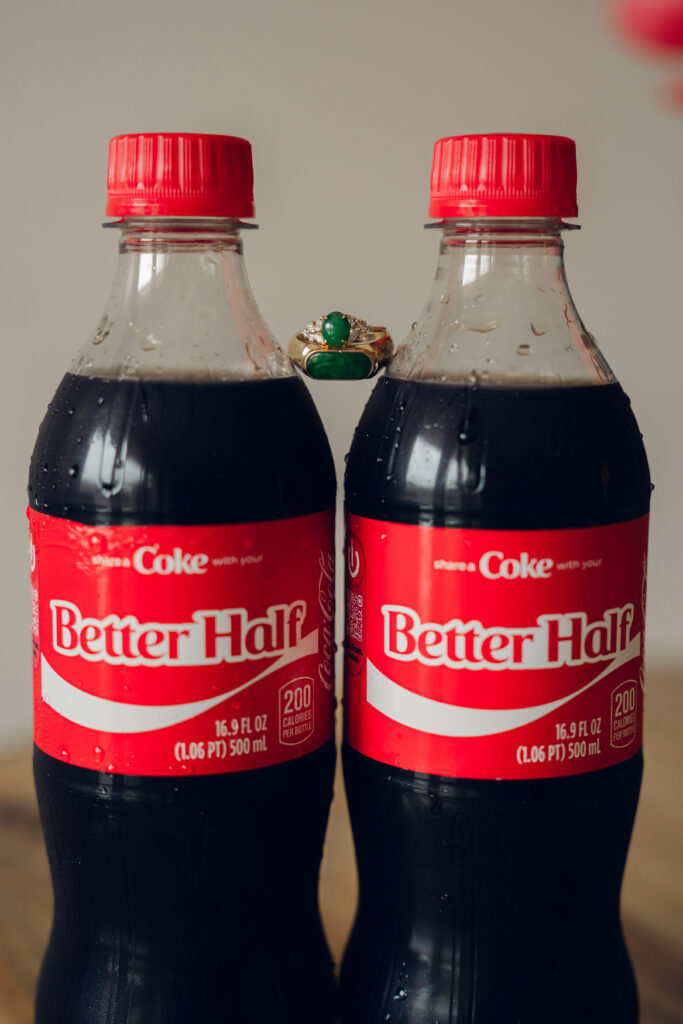 Two Coke bottles labeled “Better Half” with wedding rings balanced between the caps.