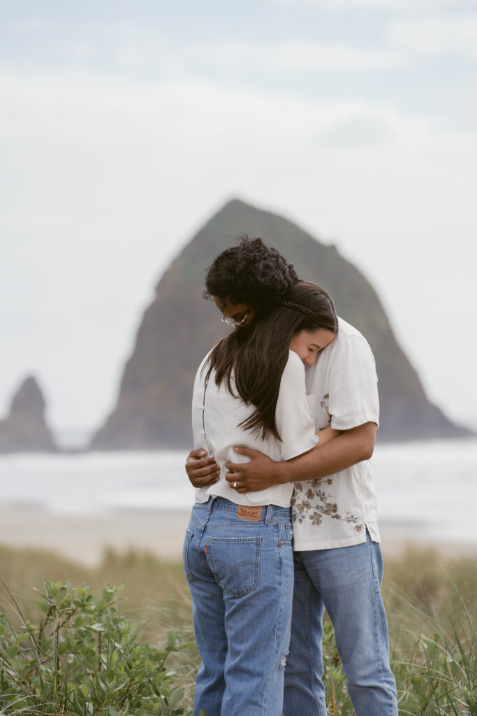 Couple embracing during their Oregon Coast elopement, with Haystack Rock softly blurred in the background.