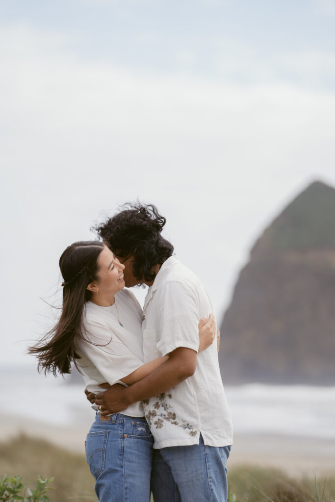 Couple embracing and smiling during their Oregon Coast elopement, with Haystack Rock in the background.